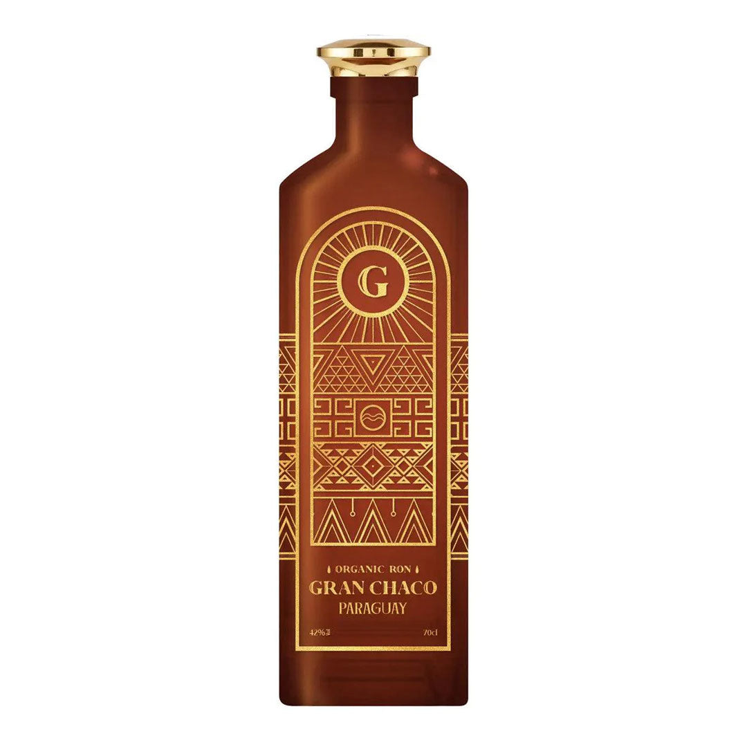 Organic Ron Gran Chaco Paraguay rum in a frosted amber bottle with gold cap and intricate Art Deco-style geometric patterns featuring a radiating 'G' logo and tribal motifs in gold on brown glass