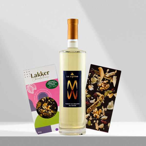 Gift set featuring a bottle of light-colored wine with a gold cap, flanked by a box of gourmet chocolates and a dark chocolate bar studded with fruit and nuts